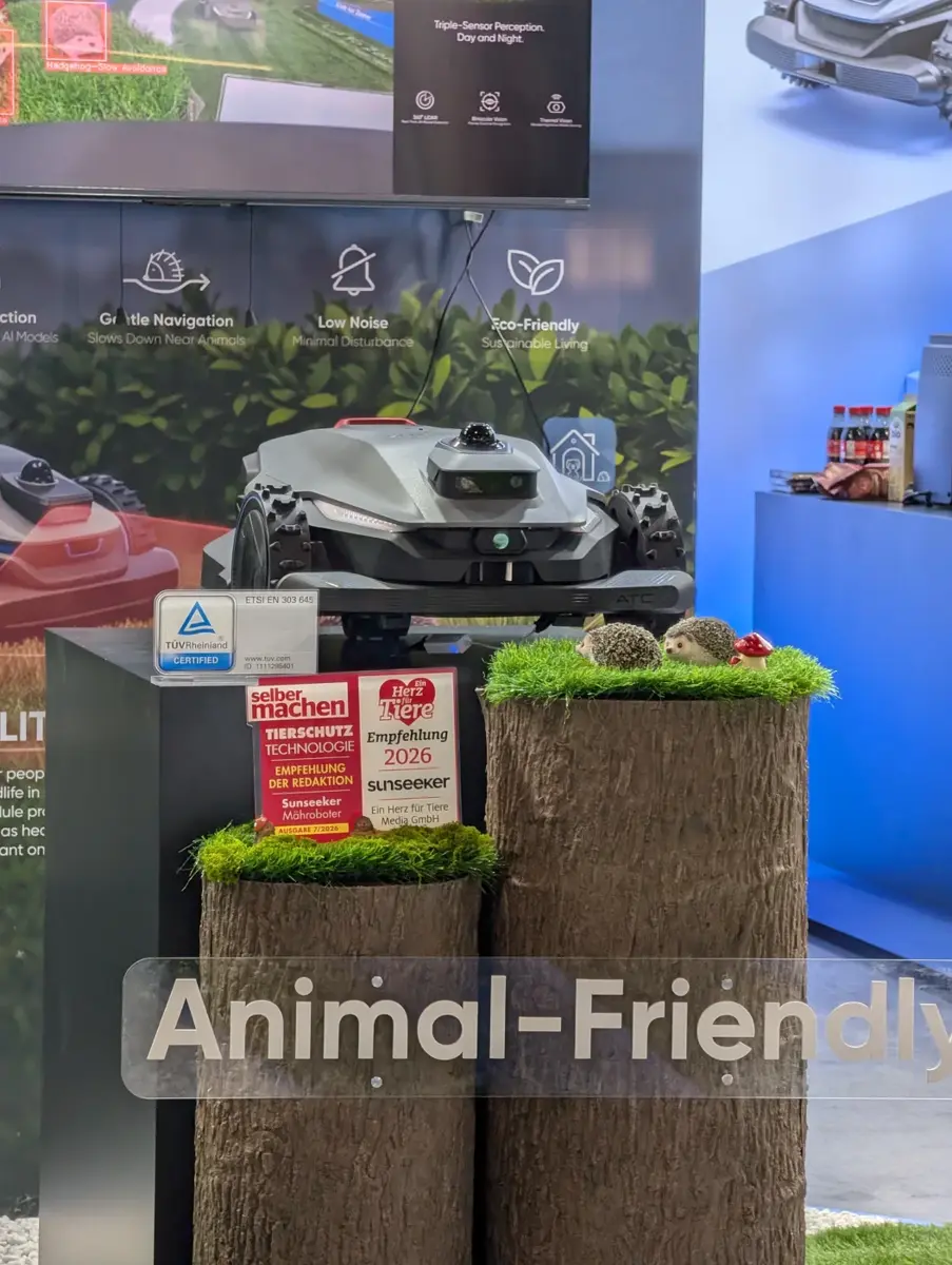 Sunseeker-Stand: ein Mähroboter auf einem Podest über Baumstumpf-Dekoration mit zwei Igelfiguren, davor Schilder mit der Tierschutz-Empfehlung der Zeitschrift selber machen, der Empfehlung 2026 von Ein Herz für Tiere und einem TÜV-Rheinland-Zertifikat, darüber die Wandtexte Gentle Navigation, Low Noise und Eco-Friendly, unten ein Schriftzug Animal-Friendly.